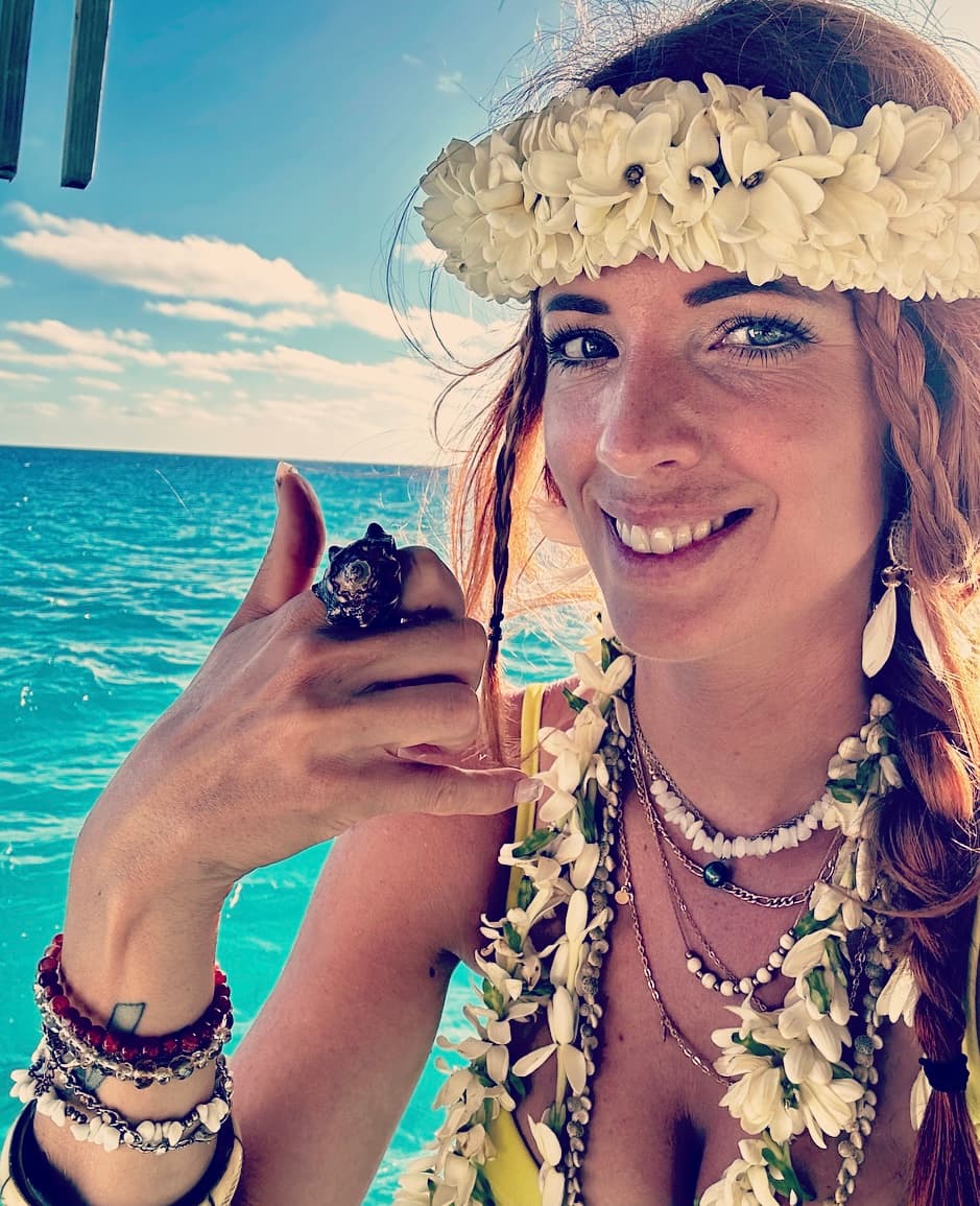 Fanny, créatrice de Pearls4Paws, portant une couronne de fleurs et présentant une bague artisanale devant le lagon de Moorea